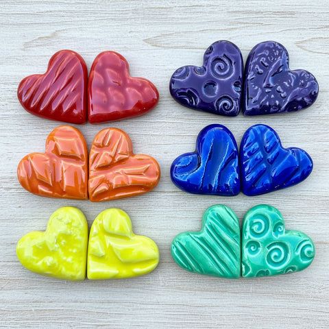 A collection of colorful ceramic hearts in various textures and colors, displayed on a wood surface.