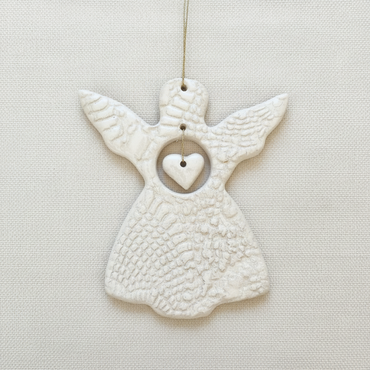 White ceramic angel ornament with a heart on a beige background