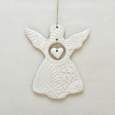 White ceramic angel ornament with a heart on a beige background