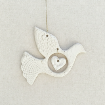 White ceramic dove with a heart on a beige fabric background