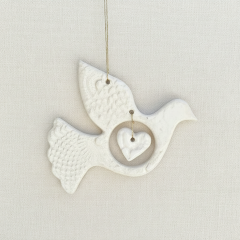 White ceramic dove with a heart on a beige fabric background