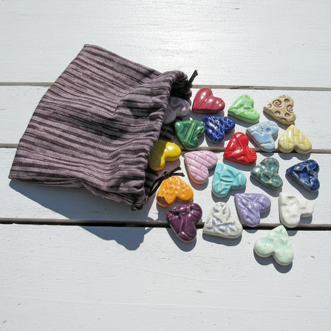Colorful heart-shaped stones on a wooden surface with a drawstring bag.