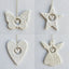 Four white ceramic ornaments shaped like a butterfly, star, heart, and angel on a fabric surface.