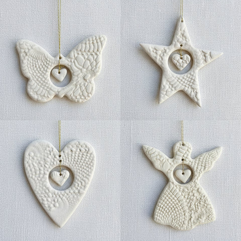 Four white ceramic ornaments shaped like a butterfly, star, heart, and angel on a fabric surface.