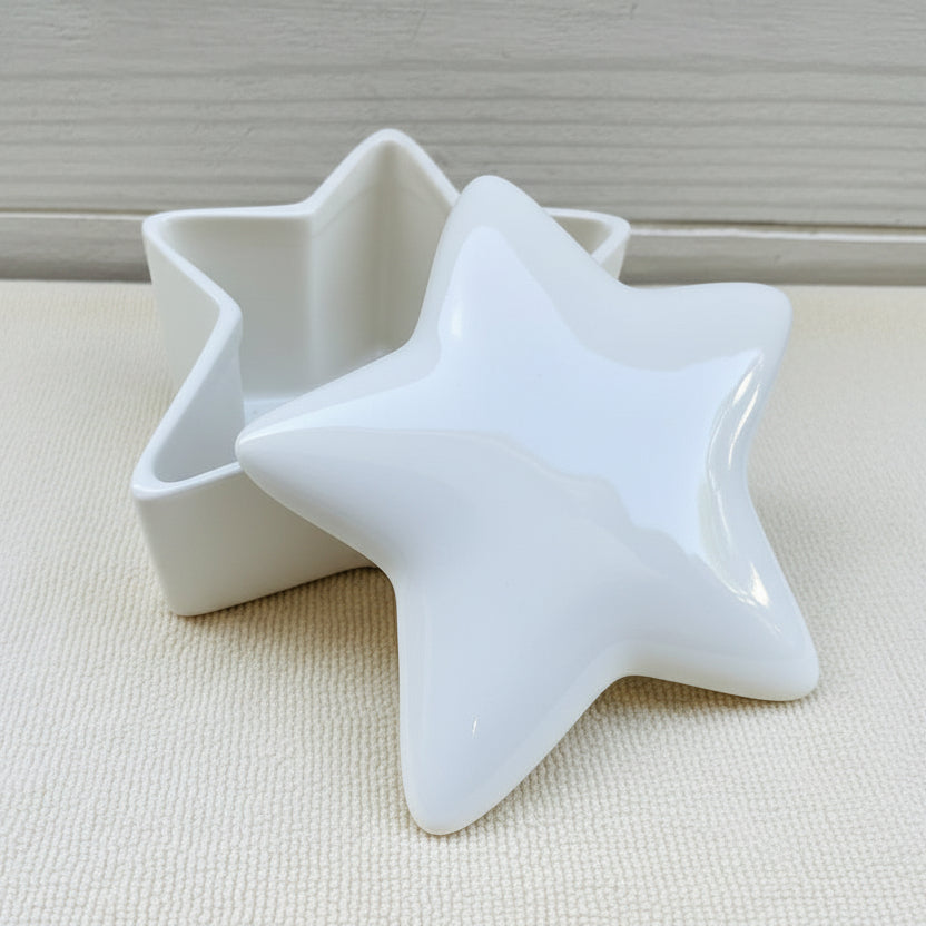 A white ceramic star-shaped urn with a candle for a temporary seal, placed on a cream textured surface.