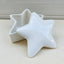 A white ceramic star-shaped urn with a candle for a temporary seal, placed on a cream textured surface.