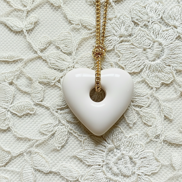 White heart-shaped pendant on a gold cord against a lace background