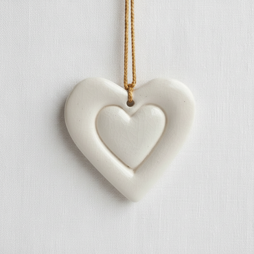 A ceramic heart with a smaller heart imprinted in the center hangs from a gold colored silk cord.