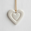 A ceramic heart with a smaller heart imprinted in the center hangs from a gold colored silk cord.