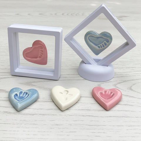 Handmade ceramic heart-shaped keepsakes in soft blue, pink and white, displayed on white wood.