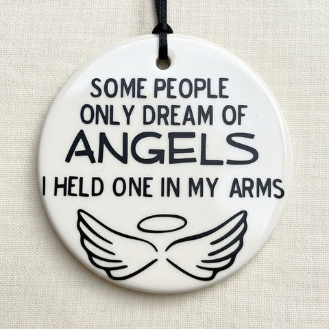 a round ornament with the quote "some people only dream of angels I held one in my arms"and angel wings