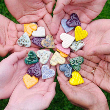 A circle of hands holding colored ceramic hearts