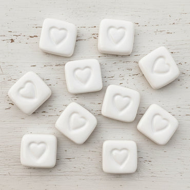 ten ceramics on white wood. ceramics are square shaped with a heart imprint in the center.